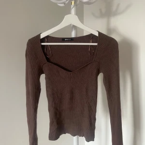 Brun ribbad tröja från Gina Tricot - Säljer en brun ribbad tröja från Gina Tricot med en v-ringad design. Tröjan har långa ärmar och en figurnära passform. 