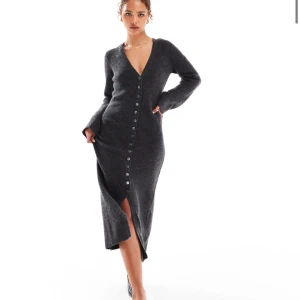 Mörkgrå stickad klänning med knappar - Elegant mörkgrå stickad klänning med v-ringning och knappar längs hela framsidan. Klänningen har långa ärmar och en stilren slits framtill, perfekt för en chic look. Den är i storlek S, passar även XS & M då den är strechig! Väldigt lik adoores klänning men är från veromoda