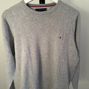Grå tröja från Tommy Hilfiger - Säljer en stilren grå tröja från Tommy Hilfiger i premium bomull. Tröjan har en liten logotyp på bröstet och rund halsringning. Perfekt för en avslappnad och snygg look.nypris 1000kr