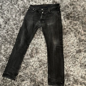 Svarta nudie jeans med slitningar - Snygga svarta nudie jeans med diskreta slitningar och en klassisk femficksdesign. De har en straight passform och är perfekta för en avslappnad stil. Jeansen har knappar och dragkedja framtill.