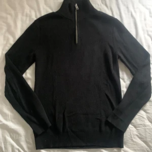 Svart stickad tröja från H&M - Säljer en stilren svart stickad tröja från H&M med dragkedja vid halsen. Perfekt för kyligare dagar med sin ribbade design och långa ärmar. En klassisk och mångsidig tröja för garderoben.