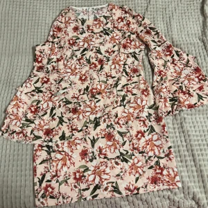 Blommig klänning med volangärmar - Säljer en vacker blommig klänning med volangärmar. Klänningen har ett färgglatt mönster i rött och grönt på en ljus bakgrund. Perfekt för en somrig look! Om ni vill se den på, skriv gärna!