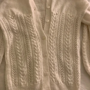 Vit stickad kofta med flätmönster - Mysig vit stickad kofta med vackert flätmönster, Långärmad design med ribbade muddar. Egensydd så inget dess värre märke, använd några gånger men inget täcken på slitage. Creme beige i färgen, sitter som en s
