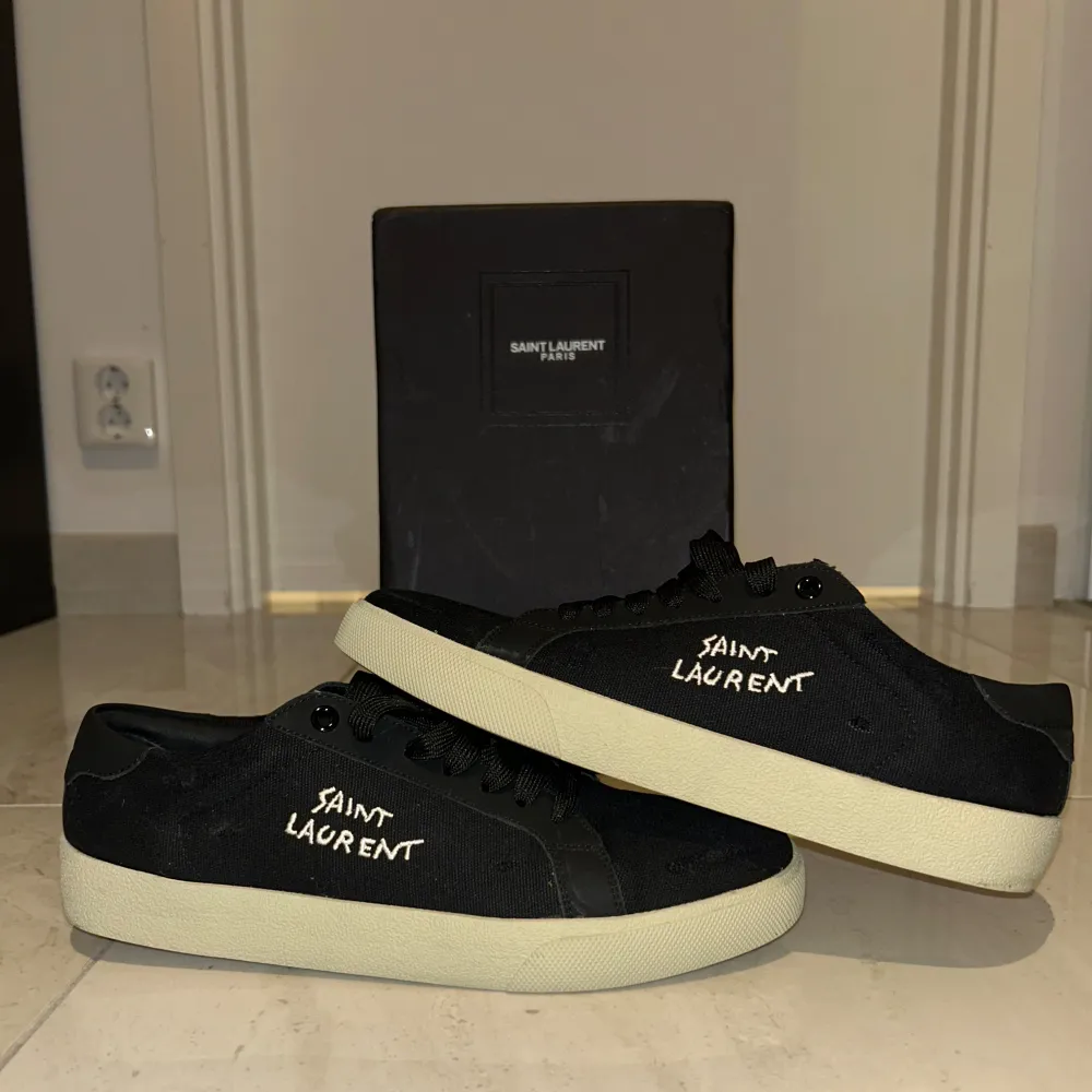 Säljer ett par snygga svarta sneakers från Saint Laurent. De har en stilren design med vit sula och Saint Laurent-loggan broderad på sidan. Perfekta för både vardag och fest! Skorna är i nyskick och kommer med originalförpackning. KVITTO FINNS!. Skor.