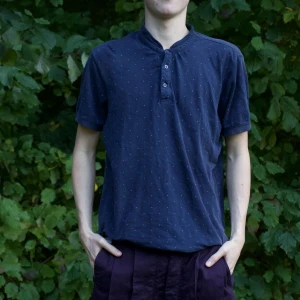 Mörkblå kortärmad t-shirt med knappar - Säljer en mörkblå kortärmad t-shirt med små prickar och knappar framtill. Perfekt för en avslappnad stil och passar bra till både vardag och fest. Skön och lätt att bära!