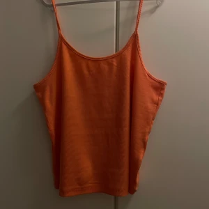  linnetopp - Säljer en snygg orange ribbad linnetopp med smala axelband. Perfekt för sommardagar eller som ett lager under en kofta. Toppen är i ett mjukt och stretchigt material som ger en bekväm passform. 