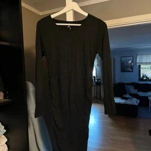 Svart långärmad klänning - Säljer en stilren svart klänning med lång ärm. Perfekt för höst och vinter, den är både bekväm och elegant. Klänningen har en tight passform som framhäver figuren. Passar bra till både vardag och festliga tillfällen . Scrunch på sidan