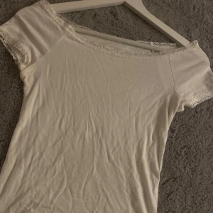 Vit topp med spetsdetaljer - Säljer en söt vit topp med spetsdetaljer vid halsringningen och ärmsluten. 