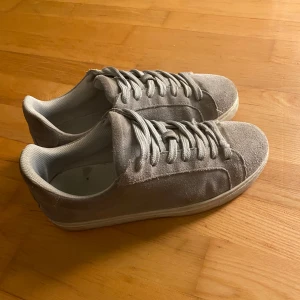 Grå mocka sneakers från Selected Homme - Snygga grå sneakers från Selected Homme i storlek 40. Skorna har en stilren design med snörning och är tillverkade i mocka. Perfekta för en avslappnad stil. Pris kan diskuteras 