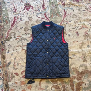 Mörkblå quiltad väst från Ralph Lauren - Säljer en snygg quiltad väst från Ralph Lauren med röd insida. Västen har knappar framtill. Bra skick. Det står XL men det är i barnstorlek, passar mer S/M