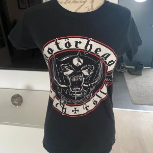 Svart Motörhead t-shirt - Cool svart t-shirt med Motörhead-tryck i vitt och rött. Perfekt för rockälskare! T-shirten har en klassisk passform och korta ärmar.