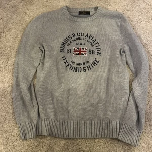 Grå tröja från Morris Gents - Säljer en stilren grå tröja från Morris Gents med tryck av Union Jack och texten 'Morris Co Aviation Oxfordshire'. Tröjan har långa ärmar och ribbade muddar vid ärmslut och nederkant. Perfekt för en avslappnad och trendig look.