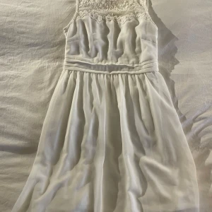 Vit klänning från Vero Moda - Säljer en elegant vit klänning från Vero Moda i storlek S. Klänningen har vackra spetsdetaljer upptill och är ärmlös med en luftig kjol. Perfekt för sommarens festligheter och studenten! 🌸
