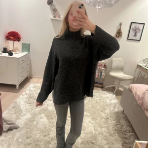 Mörkgrå stickad polotröja - Säljer en mysig mörkgrå stickad polotröja med hög krage. Tröjan har en loose passform och långa ärmar, perfekt för kyliga dagar. Den har slits längst ner