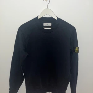 Svart tröja från Stone Island - Säljer en stilren svart tröja från Stone Island med deras ikoniska märke på ärmen. Tröjan har en klassisk rund hals och långa ärmar, perfekt för en avslappnad look. Passar bra till både jeans och chinos.