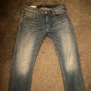 Replay Jeans - Snygga blå jeans från Replay med en klassisk femficksdesign. De har en knappgylf och en läderpatch med Replay-logga på baksidan. Perfekta för en avslappnad stil. Skön tvätt på de. Modellen heter Rocco (Comfort fit), strl 32/32. Använda 1 gång