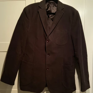 Oscar Jacobson kavaj mörkbrun - Jag säljer en snygg och stilren kavaj från Oscar Jacobson. Kavajen är i ett mörkbrunt mockaliknande tyg och är använda några få gånger men i stort sett som nyskick. 