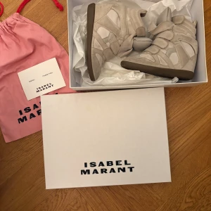 Beige sneakers med kardborreband isabel marant  - Hej! Jag säljer dessa jätte trendiga och snygga beige sneakers med hög design och flera kardborreband för en unik look. Skorna har en modern och stilren form, perfekt för dig som vill sticka ut. Tillverkade i mocka för en lyxig känsla. Skorna har en plutte röd fläck som inte syns i bilden. Skriv för fler bilder. Original pris: 5900kr låda + dusbag ingår. 