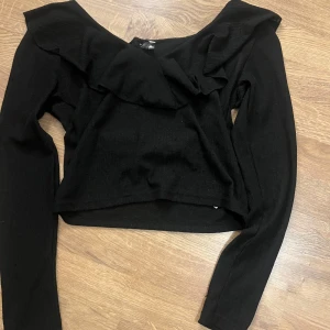 Svart tröja från NLY Trend - Snygg svart tröja från NLY Trend med volangdetaljer. Tröjan har långa ärmar och en elegant design som passar perfekt för olika tillfällen. Perfekt för dig som vill ha en stilren look.