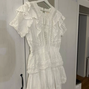 Vit klänning från byemilina - Vit klänning med volanger och spetsdetaljer. Den har korta ärmar och en vacker struktur i tyget. Är använd en gång på min studentdag! Original pris: 1800.