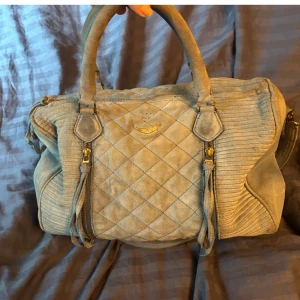 Quiltad handväska från Zadig & Voltaire - Snygg quiltad handväska i blå mocka från Zadig & Voltaire. Väskan har dragkedja och stilrena detaljer med tofsar. Perfekt för att ge din outfit en cool touch.