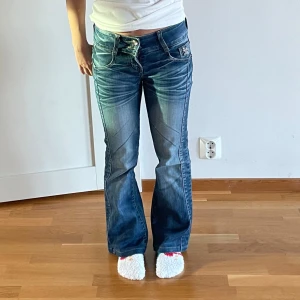 Mörkblå lågmidjade jeans - Utsvängda mörkblå jeans med detaljer på fickorna, midjemåttet rakt över är 36cm och innerbenslängden 70cm💕 den nedersta knappen har ramlat av (se bild 3)