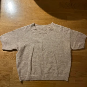 Beige stickad tröja - Säljer en mysig beige stickad tröja med korta ärmar. Tröjan har en rund halsringning och ribbade kanter. Har inte andvänts!