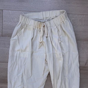 Beige linnebyxor med knytband - Snygga beige linnebyxor med elastisk midja och knytband. Byxorna har en loose passform och raka ben, vilket ger en avslappnad stil. Perfekta för varma dagar med sin lätta och luftiga känsla.