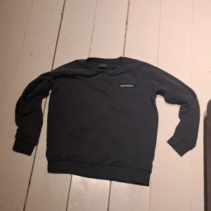Mörkblå tröja från Peak Performance - Säljer en mörkblå tröja från Peak Performance. Tröjan har långa ärmar och en enkel design med ribbade muddar vid ärmslut och nederkant. Perfekt för en avslappnad stil. Den är i bra skick men ett hål på ryggen köpare står för frakt