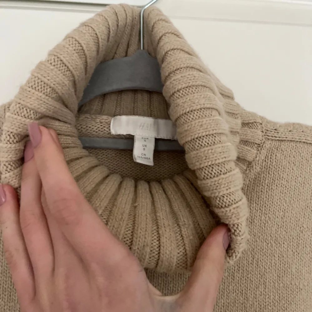 Säljer en mysig beige stickad polotröja med ribbade detaljer vid krage, ärmslut och nederkant. . Neuletakit & Villapaidat.