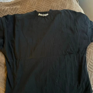Svart t-shirt från Palm Angels - Säljer en svart t-shirt från Palm Angels med stort tryck i vitt på baksidan. T-shirten har en klassisk rund hals och korta ärmar. Perfekt för en stilren look.