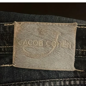 Mörkblå jeans från Jacob Cohën - Snygga mörkblå jeans från Jacob Cohën med klassisk femficksdesign och broderad logga på myntfickan. Jeansen har en stilren look med knappgylf och kontrastsömmar på bakfickorna. Ända defekten är att cohën loggan bak sitter inte fast men kan lätt sy dit igen,  den sitter men lite löst på ett hörn inte något som förstår de. Modell - 620 