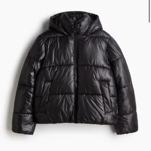 Svart pufferjacka med huva - Snygg svart pufferjacka med huva och dragkedja framtill. Jackan har en quiltad design och två praktiska fickor. Perfekt för kyliga dagar.