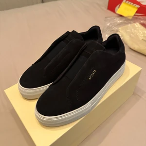 Svarta sneakers från Axel Arigato - Snygga svarta sneakers från Axel Arigato med en stilren design. Skorna har en vit sula och är tillverkade i mocka. Perfekta för en minimalistisk look. Aldrig använda med original förpackning!