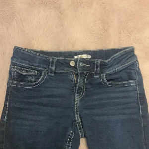 Blå jeans från Gina Tricot - Snygga blå jeans från Gina Tricot med bootcut-stil. De har en klassisk femficksdesign och framträdande vita sömmar. 