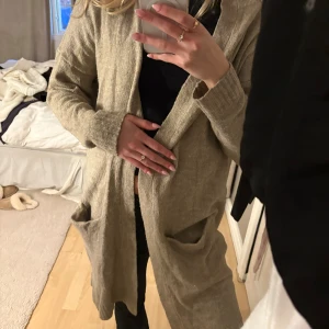 Beige långärmad kappa - Snygg beige kofta med lång ärm och stora fickor framtill. 