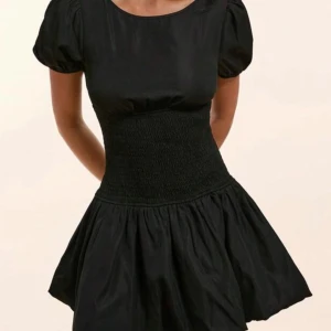Svart klänning med puffärmar - Snygg svart klänning med puffiga kortärmar och en smickrande smockad midja. Kjolen är kort och har en lätt utställd form som ger en fin silhuett. Perfekt för en stilren look.