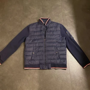 Mörkblå quiltad jacka från Ralph Lauren - Snygg mörkblå quiltad jacka från Ralph Lauren med dragkedja och broderad logga på bröstet. Jackan har långa ärmar och ribbade detaljer vid krage och ärmslut. Perfekt för kyligare dagar!