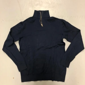 Mörkblå tröja med dragkedja från Jack & Jones - Säljer en stilren mörkblå tröja från Jack & Jones. Tröjan har en praktisk dragkedja vid halsen och är långärmad. Perfekt för billigare budget men man vill ändå ha stil 