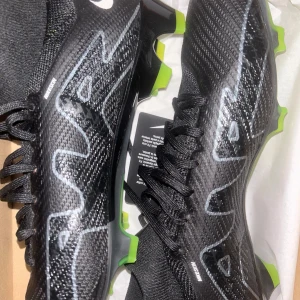 ZOOM SUPERFLY 9 PRO FG 🔥 - Snygga svarta fotbollsskor från Nike med grön sula och snörning. Skorna har en modern design med synliga Nike-loggor och är perfekta för fotbollsplanen. De har en slitstark syntetisk ovandel och en greppvänlig sula för optimalt fäste.