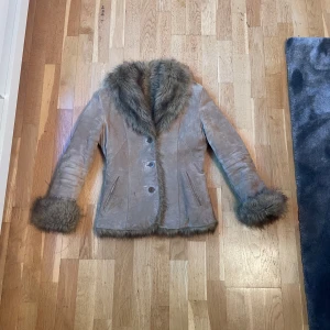 Beige mockajacka med pälsdetaljer - Säljer en snygg beige mockajacka med fluffiga pälsdetaljer på krage, ärmslut och insida. Jackan har knappar framtill och två fickor. Perfekt för kyliga dagar när du vill vara både varm och stilren.