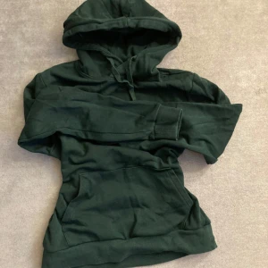 Mörkgrön hoodie från SOC - Säljer en mörkgrön hoodie från SOC i storlek XS. Den har en klassisk design med en stor ficka framtill och justerbar huva. Perfekt för en avslappnad stil.