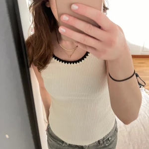 Vit ribbat linnet från H&M - Vit ribbat linne med svarta spetsdetaljer längs kanterna. 