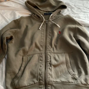   Ralph Lauren hoodie  - Säljer en beige luvtröja  från Polo Ralph Lauren med dragkedja och en broderad röd logotyp på bröstet. Tröjan har en luva  med vita snören och praktiska fickor framtill. Perfekt för en avslappnad stil. Men den är lite sliten i slutet av armarna. Priset kan diskuteras 😃