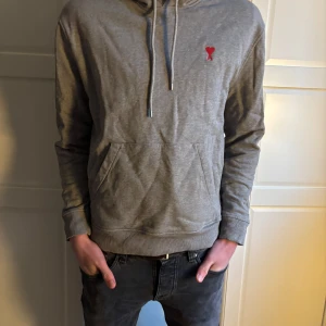 Grå hoodie från Ami Paris - Säljer en stilren grå hoodie från Ami Paris. Tröjan har en klassisk känguruficka och justerbar huva med snören. Perfekt för en avslappnad look. Nästanintill ny!