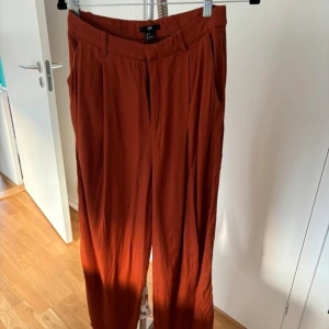 2 par old money  byxor från H&M - Säljer två par byxor från H&M i storlek S. Ett par är rostfärgade och det andra är vitt. Båda har en rak passform och är tillverkade i ett lätt och bekvämt material. Perfekta för en stilren look. Dem vita har två små obehandlade fläckar därav priset. Använda kanske en gång var. 