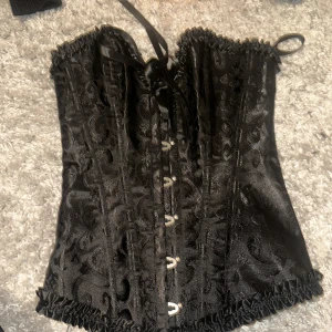 Svart sexig korsett med snörning - Elegant svart korsett med snörning framtill och vackert mönster. Perfekt för att ge en stilfull touch till din outfit. Den har en glansig finish och dekorativa kanter. Storlek xxs, aldrig använt. Slut överallt. 