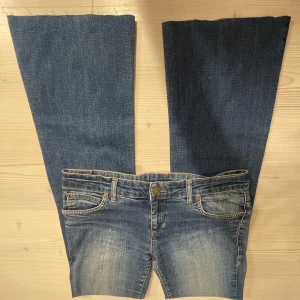 Blå Lågmidjade bootcut jeans - Snygga blå bootcut jeans med klassisk femficksdesign och slitna detaljer. Midjemåttet 39, Innerbenslängd 78, Ytterbenslängd 98 och grenmått 19. Jag är 168💗
