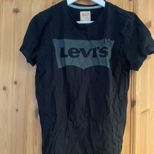 Svart t-shirt från Levi's - Säljer en svart t-shirt från Levi's med deras ikoniska logga tryckt på bröstet. T-shirten har en klassisk rund hals och korta ärmar. Perfekt för en avslappnad stil.