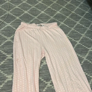 Rosa mjukisbyxor med hjärt mönster - Säljer ett par rosa mjukisbyxor med vita små hjärtan. Byxorna har en elastisk midja för extra komfort. Perfekta för en avslappnad dag hemma eller som mysplagg.